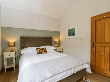 A bedroom with a double bed flanked by two nightstands with lamps and a wooden door at The Barn at Daubeneys Colerne