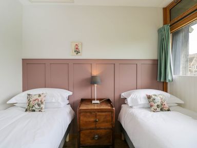 A bedroom with two single beds a wooden nightstand and a window with green curtains at The Barn at Daubeneys Colerne