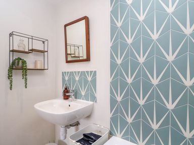 A bathroom with a white sink a wooden framed mirror geometric blue and white tiles and a wall shelf with decor at The Barn at Daubeneys Colerne