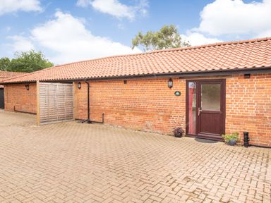 Brick building with a tiled roof and a brown door with plants on a paved area at The Hen House in Diss near Gissing