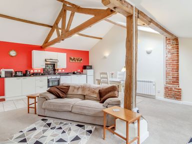 An open plan living space with a kitchen and dining area including a beige sofa with cushions and wooden beams at The Hen House in Diss near Gissing