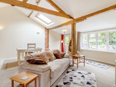 A living room with a sofa and dining table under wooden beams at The Hen House in Diss near Gissing