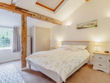 A bedroom with a bed bedside tables lamps wooden beam and a window at The Hen House in Diss near Gissing