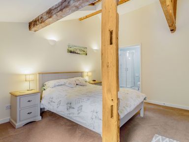 A bedroom with a double bed bedside tables lamps wooden beams and an ensuite bathroom at The Hen House in Diss near Gissing
