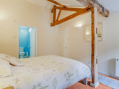 A bedroom with a bed pillows wooden beam and an adjoining bathroom at The Hen House in Diss near Gissing