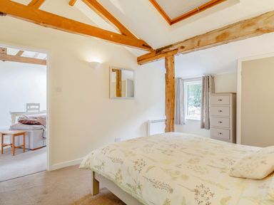 A bedroom with a bed chest of drawers mirror and exposed wooden beams at The Hen House in Diss near Gissing