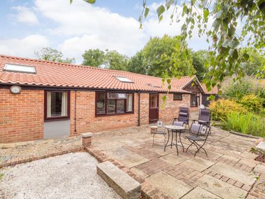 A brick house with a tiled roof and patio furniture on a stone paved patio at The Hen House in Diss near Gissing