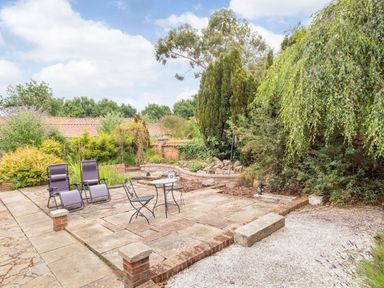 An outdoor patio area with two reclining chairs a small round table with two chairs surrounded by plants and trees at The Hen House in Diss near Gissing