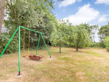 A green swing set with two swings on a grassy area surrounded by trees at The Hen House in Diss near Gissing