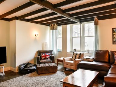 A living room with leather and fabric chairs a coffee table and windows at Tower House in Boscastle