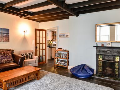 A living room with a leather sofa an armchair a wooden coffee table a bookshelf and a fireplace at Tower House in Boscastle