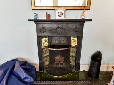 A black fireplace with decorative tiles and a screen surrounded by a blue beanbag and a black container at Tower House in Boscastle