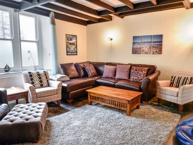 A living room with a brown sectional sofa two armchairs a wooden coffee table and a gray rug at Tower House in Boscastle