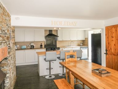 A kitchen with white cabinets a black stove a wooden dining table with chairs and stools at Tower House in Boscastle