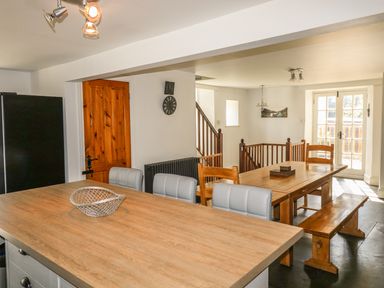 A dining area with wooden table wooden bench chairs and a kitchen island with light grey stools at Tower House in Boscastle