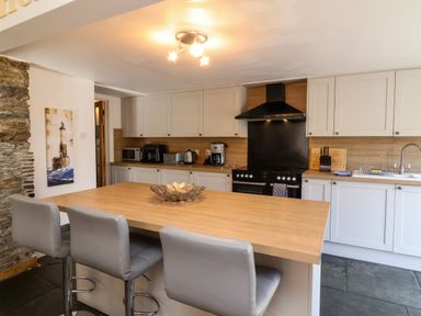 A kitchen with a wooden island and three grey chairs white cabinets and black stove at Tower House in Boscastle