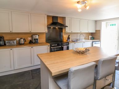 A kitchen with white cabinets wooden countertops a black stove and oven a wooden island with grey chairs at Tower House in Boscastle