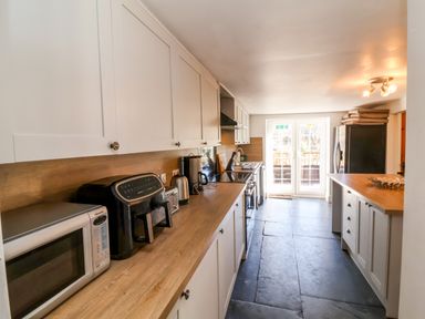 A kitchen with white cabinets wooden countertops appliances and a door leading outside at Tower House in Boscastle