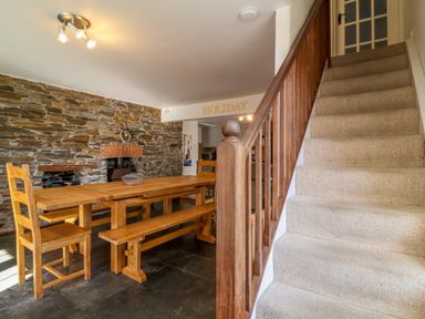 A dining area with a wooden table bench and chairs next to a stone wall and a carpeted staircase at Tower House in Boscastle