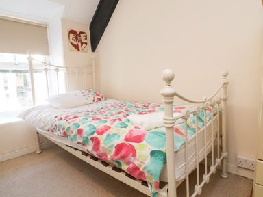 A bedroom with a single bed with a white metal frame colorful bedding a window and a wall decoration at Tower House in Boscastle