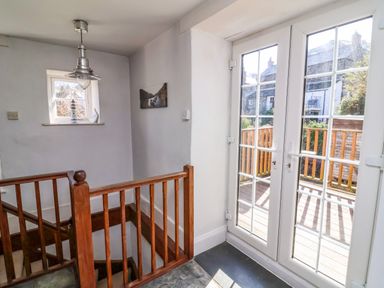 A stairwell with wooden railing next to glass double doors leading to a balcony at Tower House in Boscastle