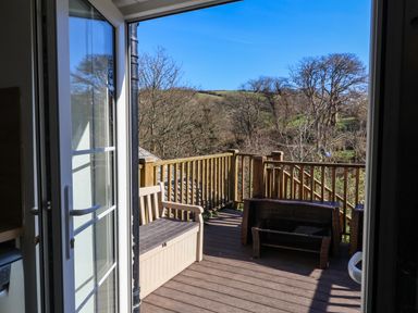 A balcony with a wooden bench and table set overlooking trees and hills at Tower House in Boscastle