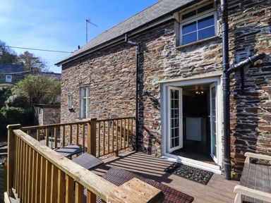 A wooden deck with seating outside a stone house with open glass doors at Tower House in Boscastle