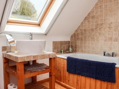 A bathroom with a wooden bathtub and tiled wall under a skylight window at Cross Syke Barn in Loxhore near Barnstaple