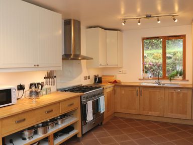 A kitchen with wooden cabinets a gas stove a microwave and a window with plants at Cross Syke Barn in Loxhore near Barnstaple