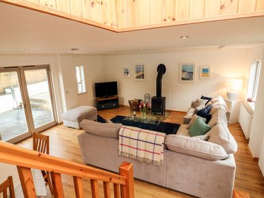 A living room with a sectional sofa a glass coffee table a wood stove and a TV at Cross Syke Barn in Loxhore near Barnstaple