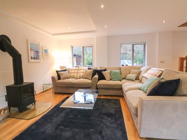 A living room with beige sofas and cushions a black wood stove and a glass coffee table at Cross Syke Barn in Loxhore near Barnstaple