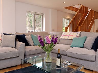A living room with a glass coffee table a vase of flowers a bottle of wine and a sectional sofa at Cross Syke Barn in Loxhore near Barnstaple