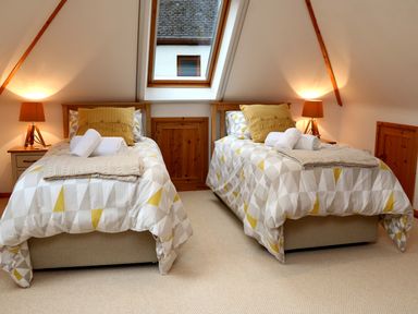A bedroom with two single beds each with a yellow pillow folded towels and bedside lamps at Cross Syke Barn in Loxhore near Barnstaple