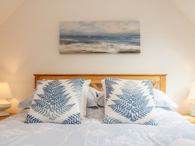 A bedroom with a wooden headboard two pillows with leaf patterns two lamps and a beach painting at Cross Syke Barn in Loxhore near Barnstaple