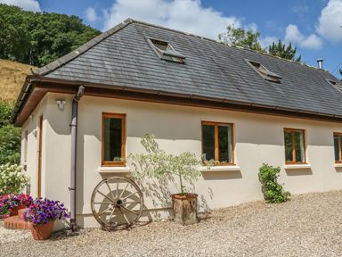 Exterior view of a building with windows a slate roof potted plants and a wooden wagon wheel at Cross Syke Barn in Loxhore near Barnstaple