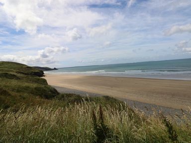 A beach with sand and waves next to a grassy hillside at Harmon Vale in Solva