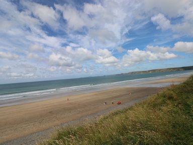 A beach with sand and waves under a partly cloudy sky with grassy dunes at Harmon Vale in Solva