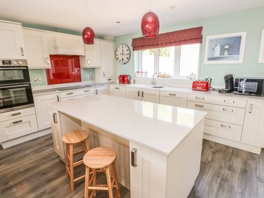 A kitchen with white cabinets two wooden stools a white island countertop red hanging lights and red kitchen appliances at Harmon Vale in Solva