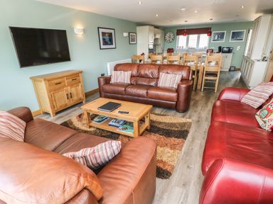 A living room with leather sofas a wooden coffee table and a dining table with chairs at Harmon Vale in Solva