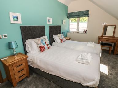 A bedroom with two single beds bedside tables a window and a dressing table at Harmon Vale in Solva