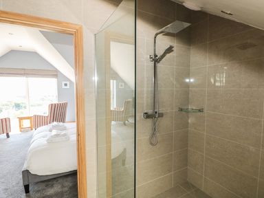 A bathroom with a glass shower enclosure and a bedroom with a bed and two armchairs at Harmon Vale in Solva