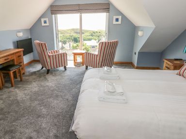 A bedroom with two beds a wooden desk two striped armchairs and a window with a view at Harmon Vale in Solva