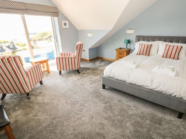 A bedroom with a bed two striped armchairs a small wooden table and a large window at Harmon Vale in Solva