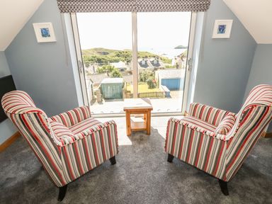 A sitting area with two striped armchairs and a small wooden table by a large window overlooking houses and greenery at Harmon Vale in Solva