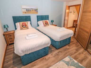 A bedroom with two single beds with owl pillows bedside tables lamps and a painting at Harmon Vale in Solva