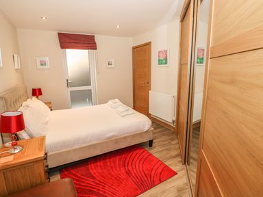 A bedroom with a double bed two red lamps a red rug a wooden wardrobe with mirrored doors and a wooden door at Harmon Vale in Solva