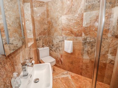 A bathroom with a white sink a toilet a towel holder with a white towel and stone tile walls at Harmon Vale in Solva