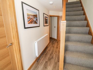 A hallway with wooden doors a carpeted staircase photos on the wall and a radiator at Harmon Vale in Solva