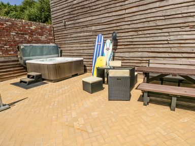 An outdoor patio area with a hot tub surfboards garden furniture and a picnic table at Harmon Vale in Solva