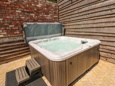 An outdoor hot tub with water and steps beside wooden and brick walls at Harmon Vale in Solva